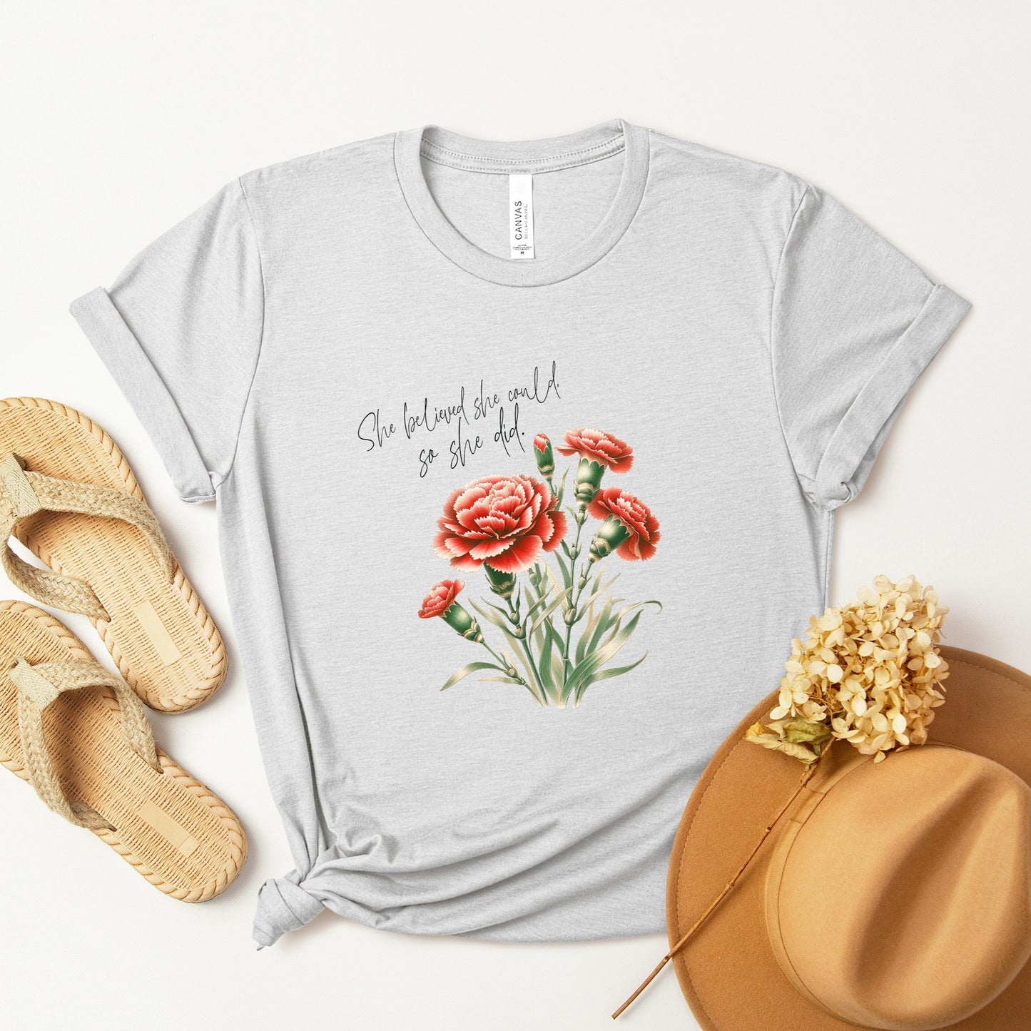 A t-shirt featuring a beautiful carnation for January with the quote “She believed she could, so she did.” Perfect for January birthdays and floral art lovers. Comfortable and stylish for casual outings or celebrations. Bella+Canvas 3001 t-shirt in ash. ReadyShirtAim.com