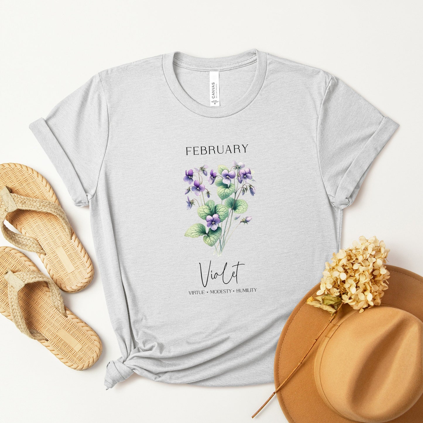 A t-shirt featuring a beautiful violet for February with traits Virtue, Modesty, Humility. Perfect for February birthdays and floral art lovers. Comfortable and stylish for casual outings or celebrations. Bella+Canvas 3001 t-shirt in ash. ReadyShirtAim.com