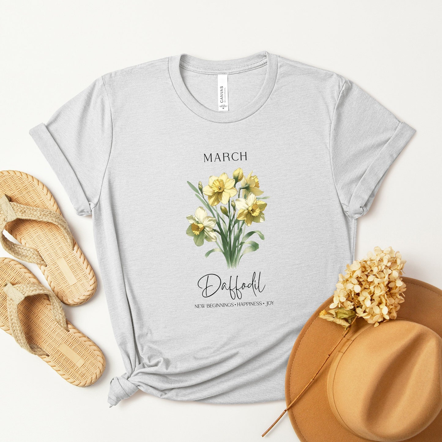 A t-shirt featuring a beautiful daffodil for March with traits New Beginnings, Happiness, Joy. Perfect for March birthdays and floral art lovers. Comfortable and stylish for casual outings or celebrations. Bella+Canvas 3001 t-shirt in ash. ReadyShirtAim.com