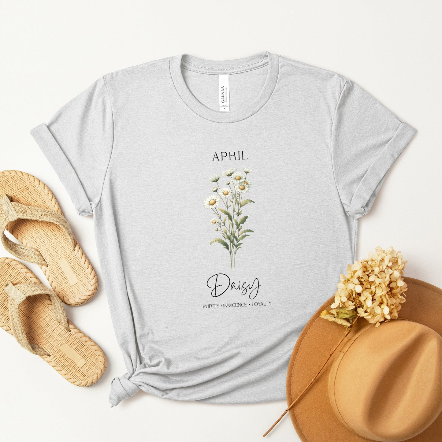 A t-shirt featuring a beautiful daisy for April with traits Purity, Innocence, Loyalty. Perfect for April birthdays and floral art lovers. Comfortable and stylish for casual outings or celebrations. Bella+Canvas 3001 t-shirt in ash. ReadyShirtAim.com