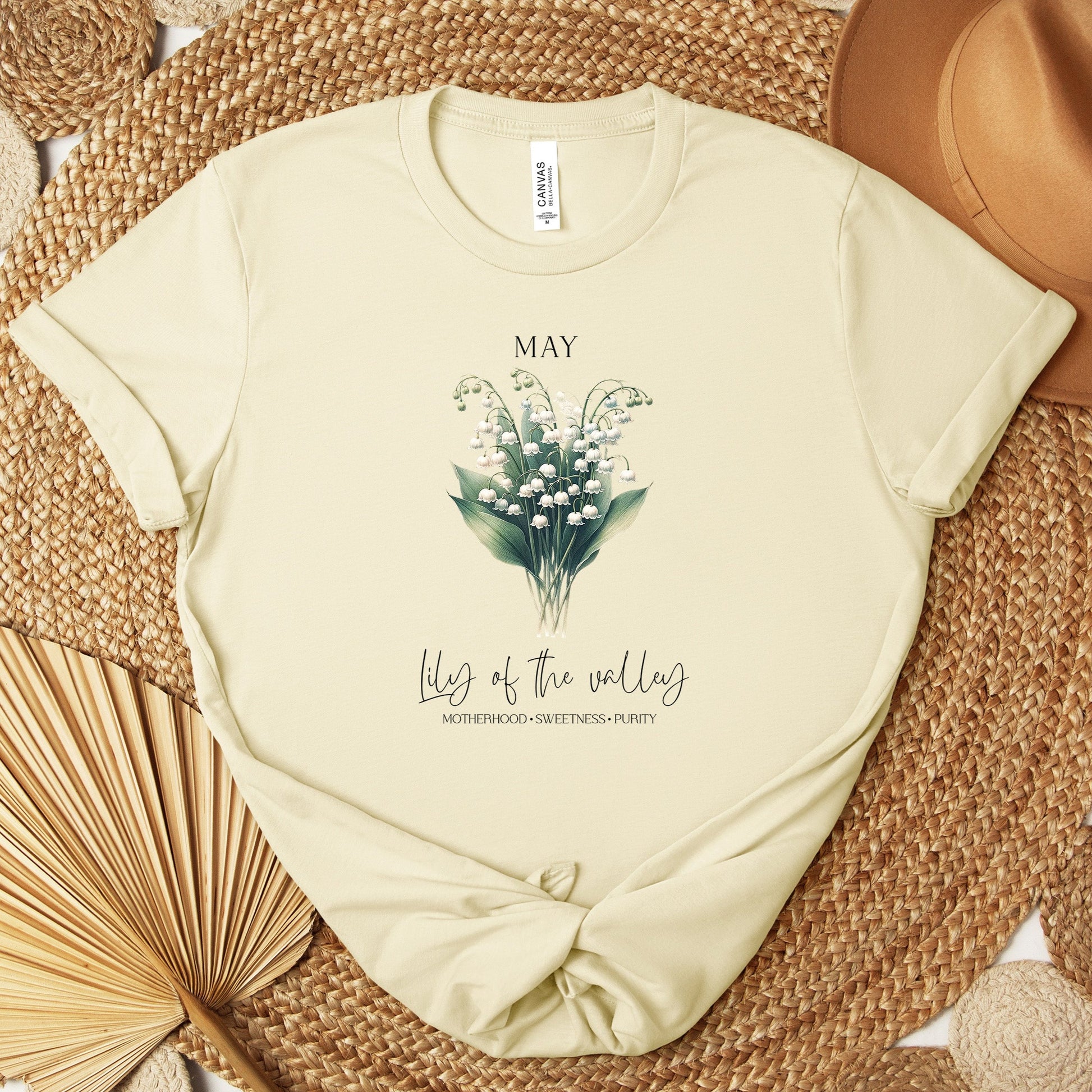 A t-shirt featuring a beautiful Lily of the Valley for May with traits Motherhood, Sweetness, Purity. Perfect for May birthdays and floral art lovers. Comfortable and stylish for casual outings or celebrations. Bella+Canvas 3001 t-shirt in natural. ReadyShirtAim.com