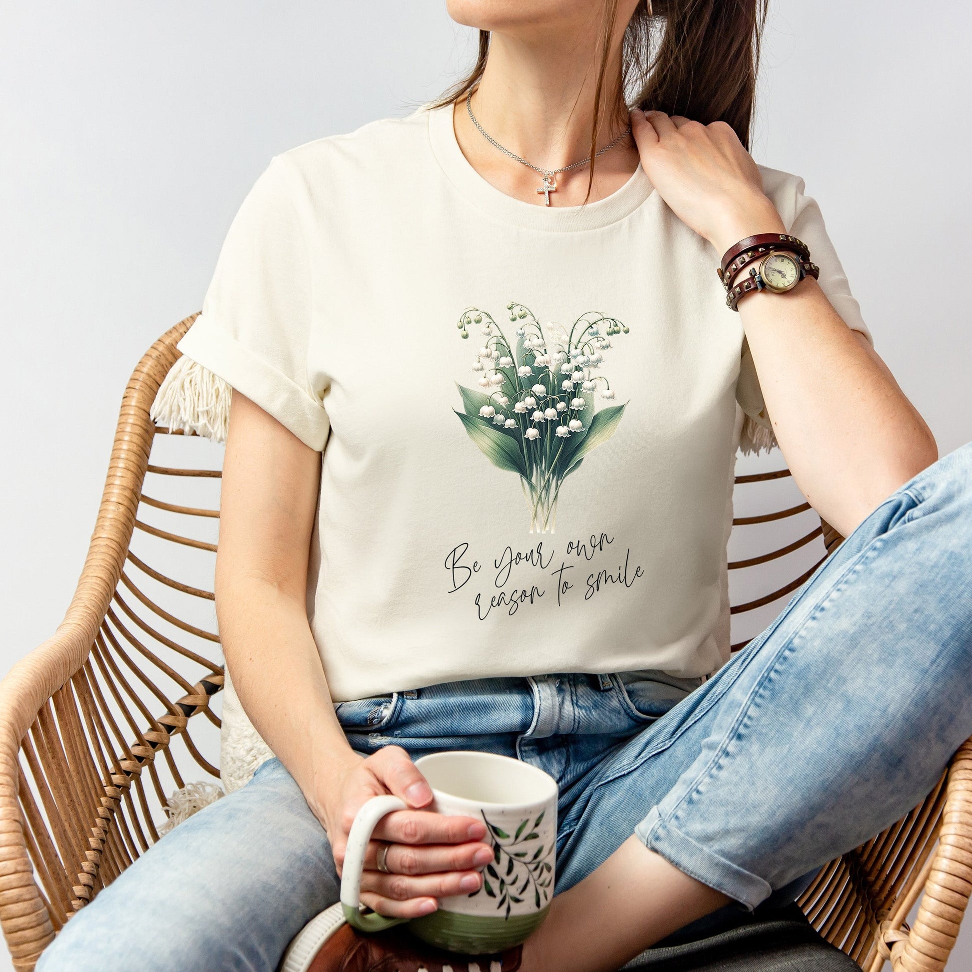 A t-shirt featuring a beautiful Lily of the Valley for May with the quote “Be your own reason to smile.” Perfect for May birthdays and floral art lovers. Comfortable and stylish for casual outings or celebrations. Bella+Canvas 3001 t-shirt in natural. ReadyShirtAim.com