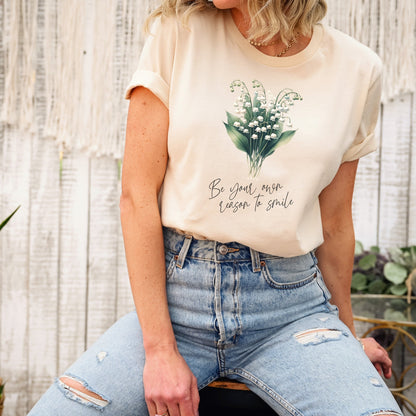 A t-shirt featuring a beautiful Lily of the Valley for May with the quote “Be your own reason to smile.” Perfect for May birthdays and floral art lovers. Comfortable and stylish for casual outings or celebrations. Bella+Canvas 3001 t-shirt in soft cream. ReadyShirtAim.com