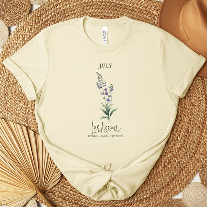 A t-shirt featuring a beautiful larkspur for July with traits Positive, Grace, First Love. Perfect for July birthdays and floral art lovers. Comfortable and stylish for casual outings or celebrations. Bella+Canvas 3001 t-shirt in natural. ReadyShirtAim.com