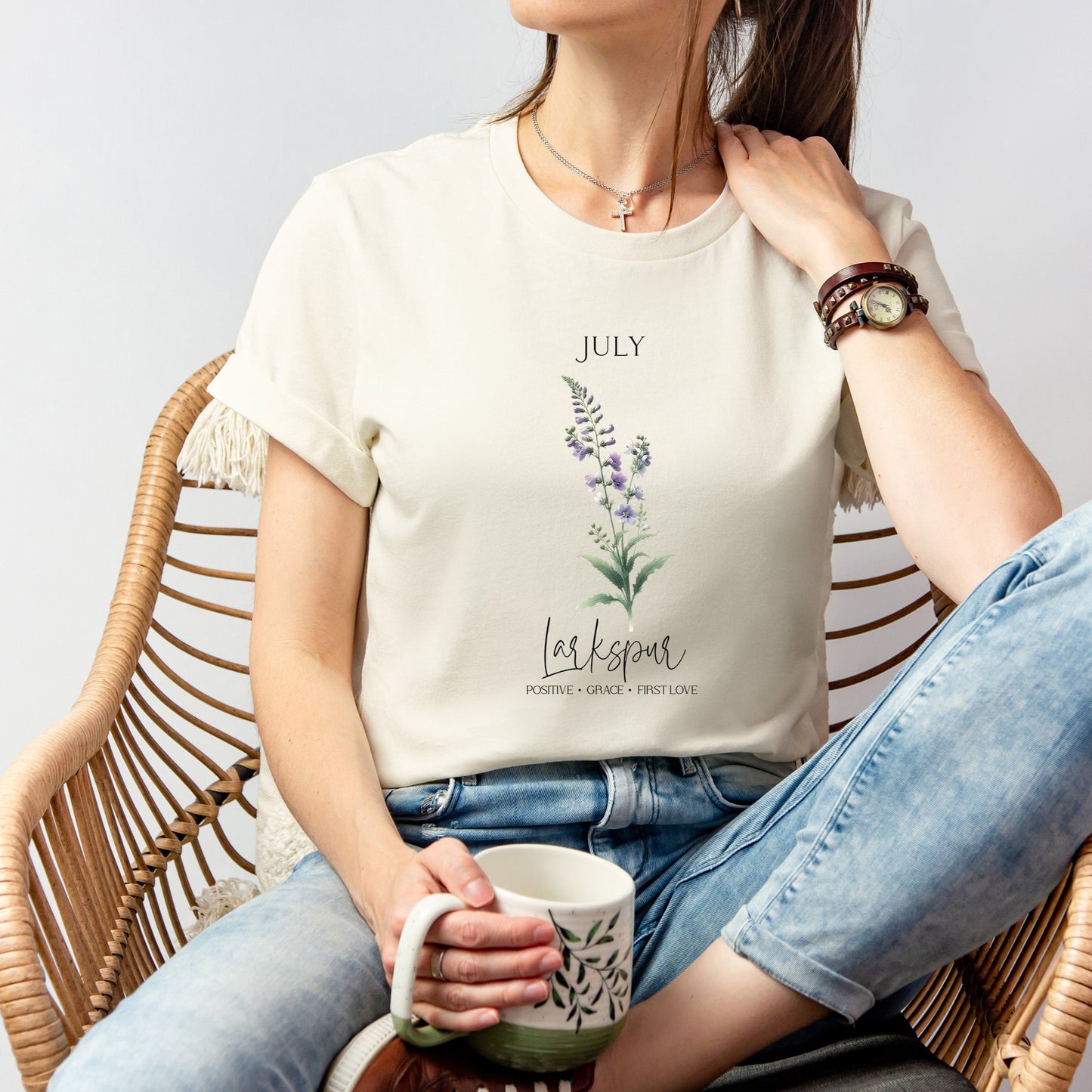 A t-shirt featuring a beautiful larkspur for July with traits Positive, Grace, First Love. Perfect for July birthdays and floral art lovers. Comfortable and stylish for casual outings or celebrations. Bella+Canvas 3001 t-shirt in natural. ReadyShirtAim.com