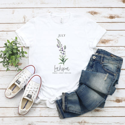 A t-shirt featuring a beautiful larkspur for July with traits Positive, Grace, First Love. Perfect for July birthdays and floral art lovers. Comfortable and stylish for casual outings or celebrations. Bella+Canvas 3001 t-shirt in white. ReadyShirtAim.com