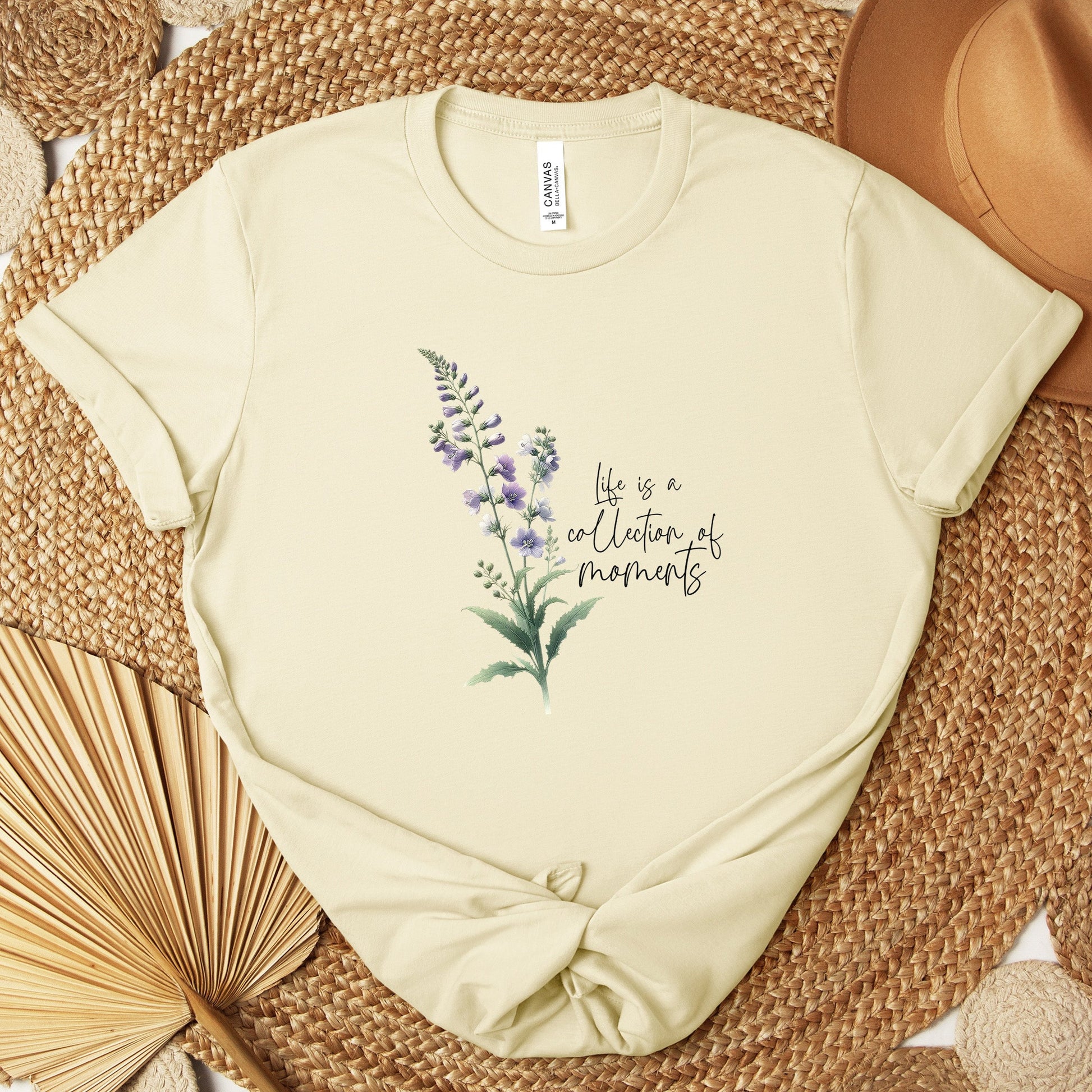 A t-shirt featuring a beautiful larkspur for July with the quote “Life is a collection of moments.” Perfect for July birthdays and floral art lovers. Comfortable and stylish for casual outings or celebrations. Bella+Canvas 3001 t-shirt in natural. ReadyShirtAim.com