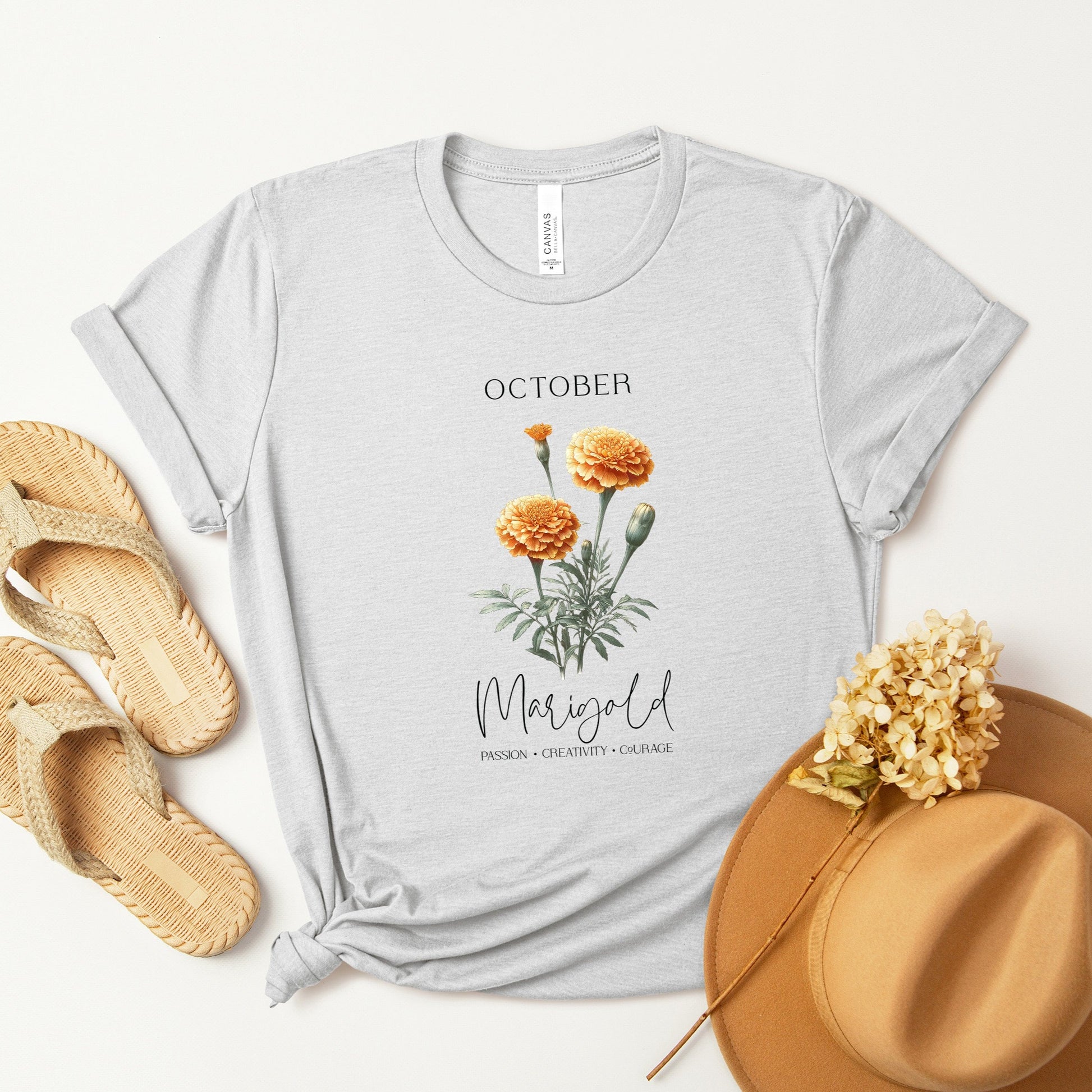 A t-shirt featuring a beautiful marigold for October with traits Passion, Creativity, Courage. Perfect for October birthdays and floral art lovers. Comfortable and stylish for casual outings or celebrations. Bella+Canvas 3001 t-shirt in ash. ReadyShirtAim.com