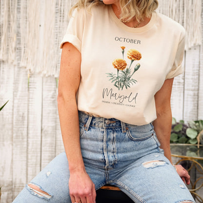 A t-shirt featuring a beautiful marigold for October with traits Passion, Creativity, Courage. Perfect for October birthdays and floral art lovers. Comfortable and stylish for casual outings or celebrations. Bella+Canvas 3001 t-shirt in soft cream. ReadyShirtAim.com