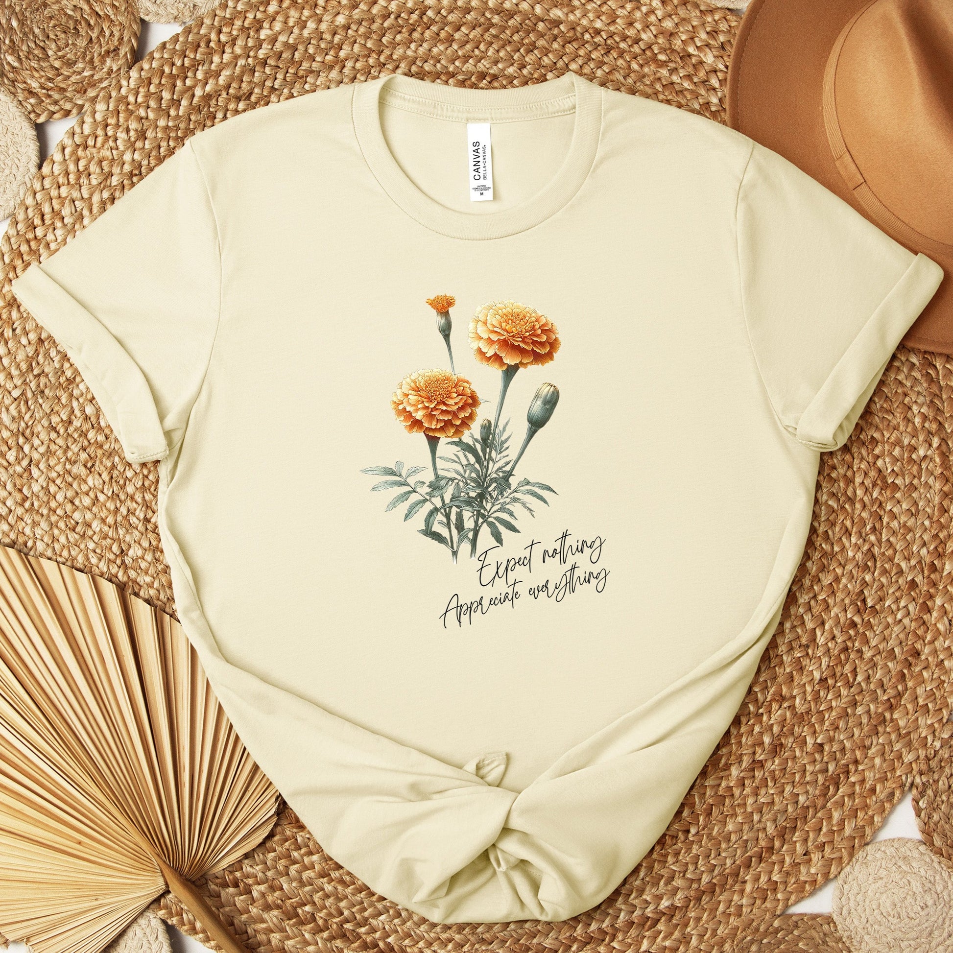 A t-shirt featuring a beautiful marigold for October with the quote “Expect nothing, appreciate everything.” Perfect for October birthdays and floral art lovers. Comfortable and stylish for casual outings or celebrations. Bella+Canvas 3001 t-shirt in natural. ReadyShirtAim.com