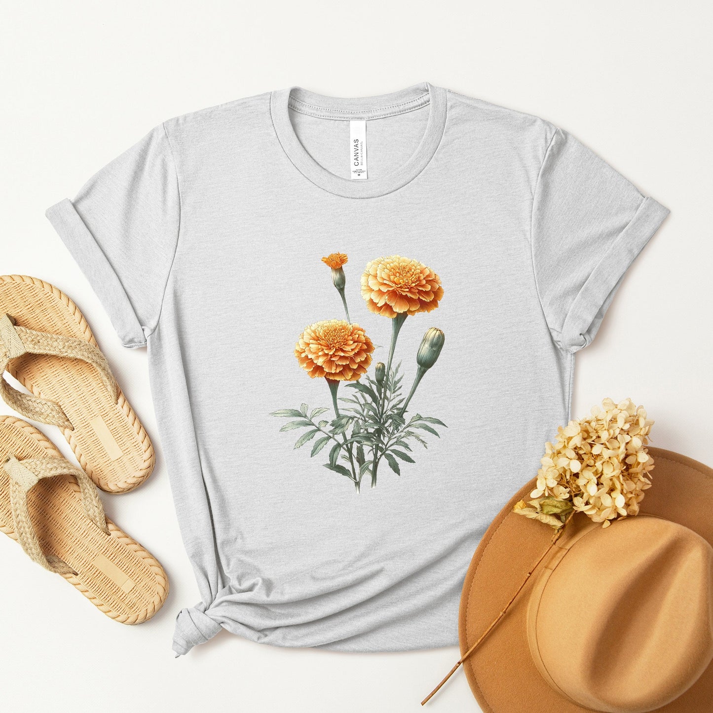 A t-shirt featuring a beautiful marigold for October. Perfect for October birthdays and floral art lovers. Comfortable and stylish for casual outings or celebrations. Bella+Canvas 3001 t-shirt in ash. ReadyShirtAim.com