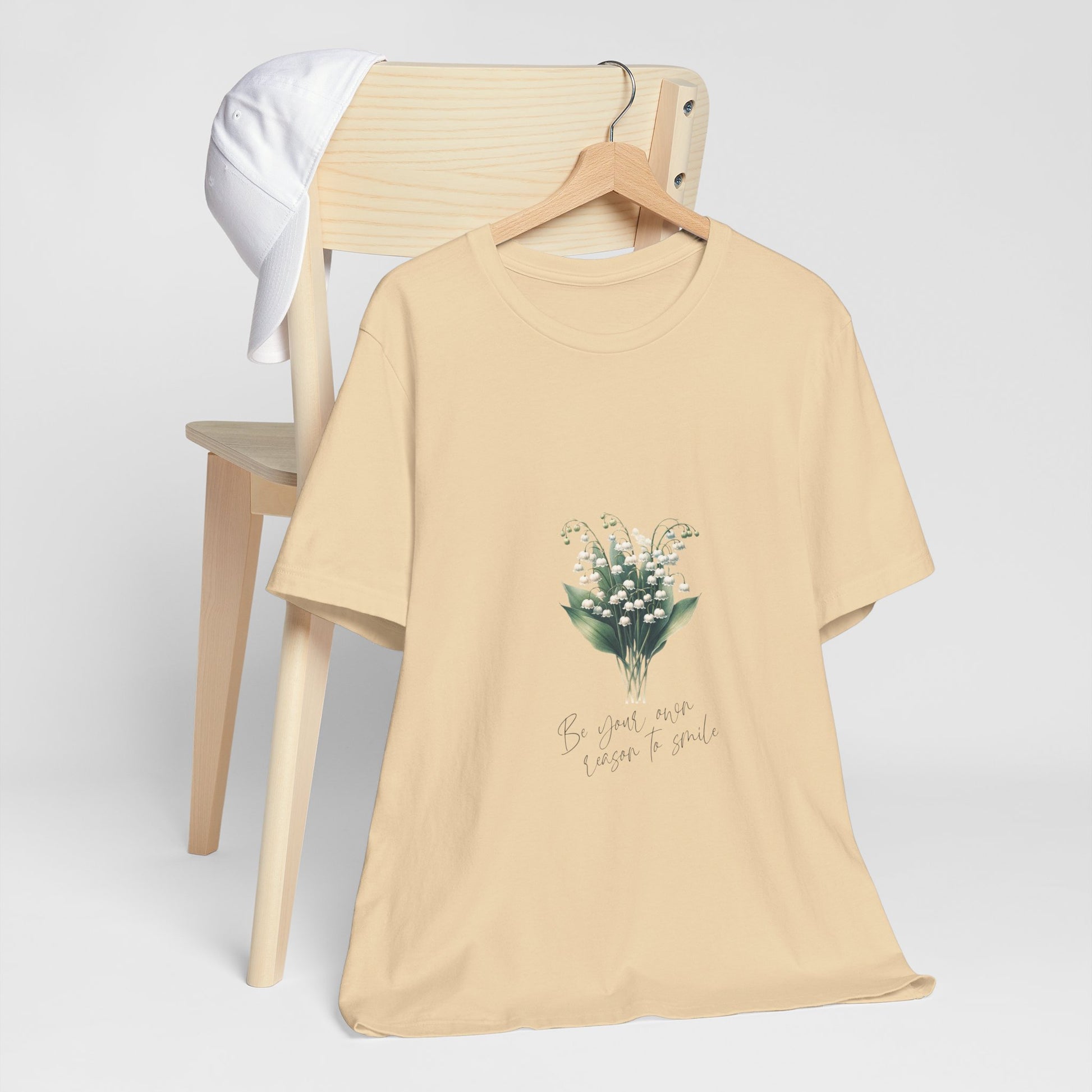 A t-shirt featuring a beautiful Lily of the Valley for May with the quote “Be your own reason to smile.” Perfect for May birthdays and floral art lovers. Comfortable and stylish for casual outings or celebrations. Bella+Canvas 3001 t-shirt in soft cream. ReadyShirtAim.com