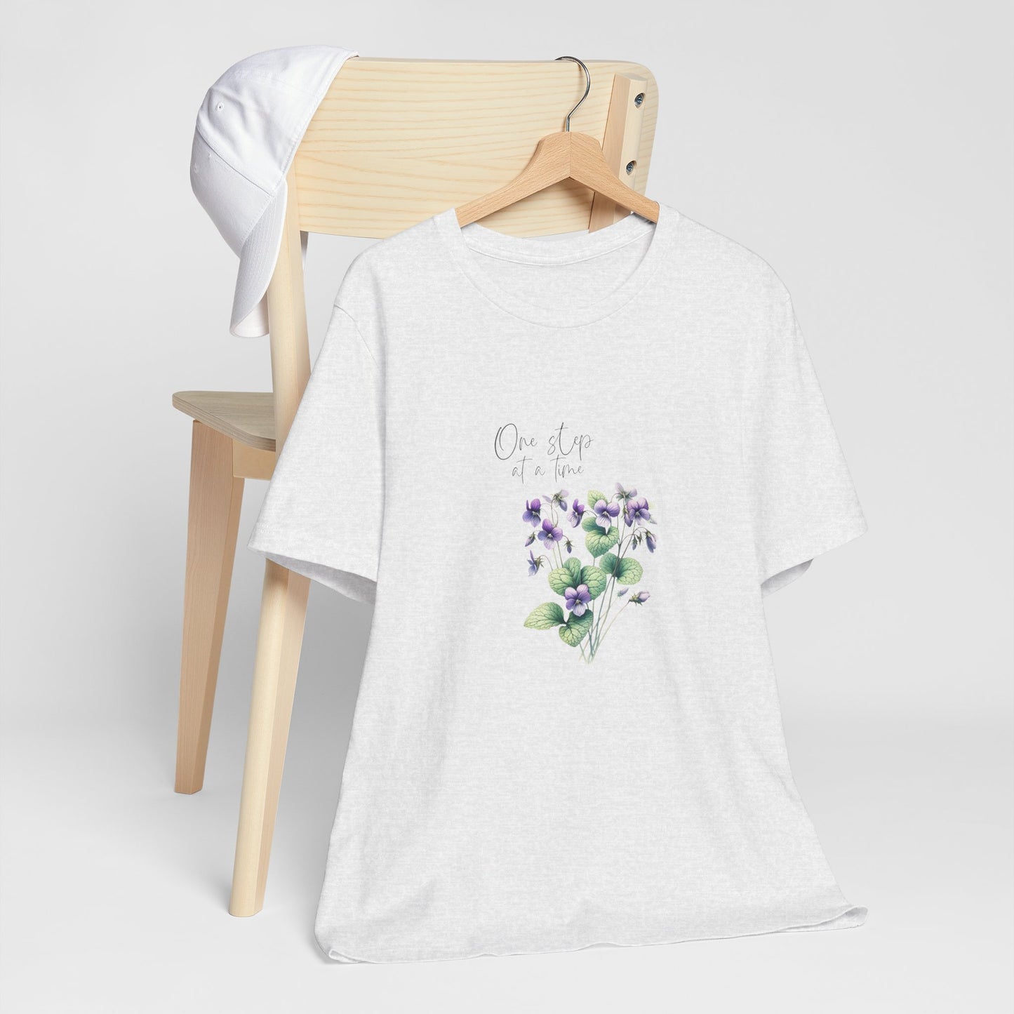 A t-shirt featuring a beautiful violet for February with the quote “One step at a time.” Perfect for February birthdays and floral art lovers. Comfortable and stylish for casual outings or celebrations. Bella+Canvas 3001 t-shirt in ash. ReadyShirtAim.com