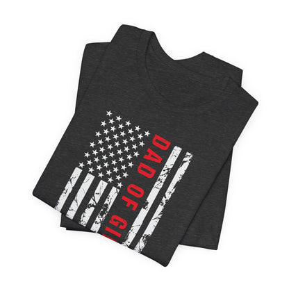 A dark-colored t-shirt featuring a grungy American flag design with the text "Dad of girls #outnumbered" in white and red. Perfect for Father's Day, Fourth of July, and patriotic dads who love humor. Comfortable and stylish for casual wear. Bella+Canvas 3001 t-shirt in dark grey heather. ReadyShirtAim.com