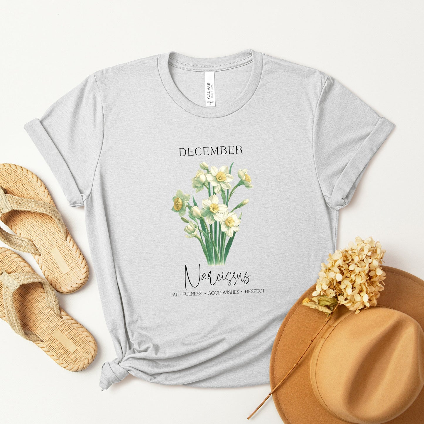 A t-shirt featuring a beautiful narcissus for December with traits Faithfulness, Good Wishes, Respect. Perfect for December birthdays and floral art lovers. Comfortable and stylish for casual outings or celebrations. Bella+Canvas 3001 t-shirt in ash. ReadyShirtAim.com