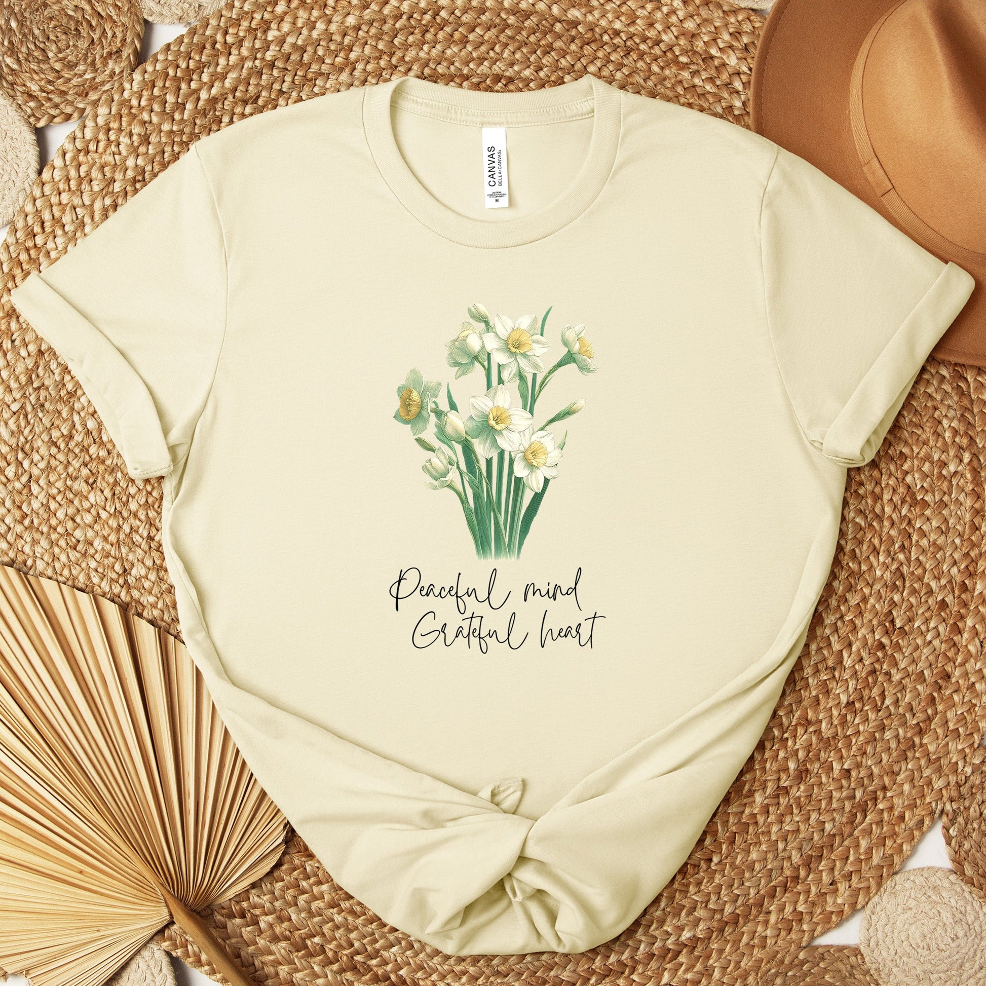 A t-shirt featuring a beautiful narcissus for December with the quote “Peaceful mind, grateful heart.” Perfect for December birthdays and floral art lovers. Comfortable and stylish for casual outings or celebrations. Bella+Canvas 3001 t-shirt in natural. ReadyShirtAim.com