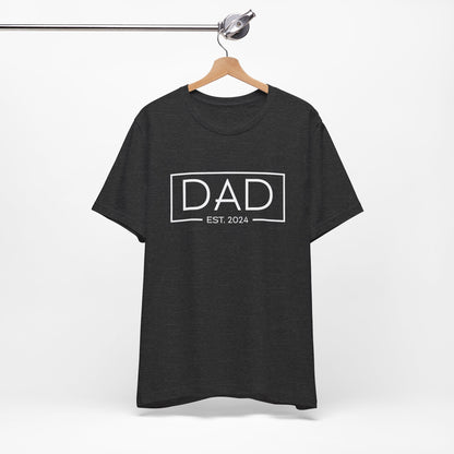 A dark t-shirt featuring the text "Dad Est. 2024" in a modern font, perfect for new fathers. Made from soft, breathable cotton, this shirt is an ideal gift for Father's Day or to celebrate a newborn's arrival. Available in multiple colors and sizes. Bella+Canvas 3001 t-shirt. ReadyShirtAim.com