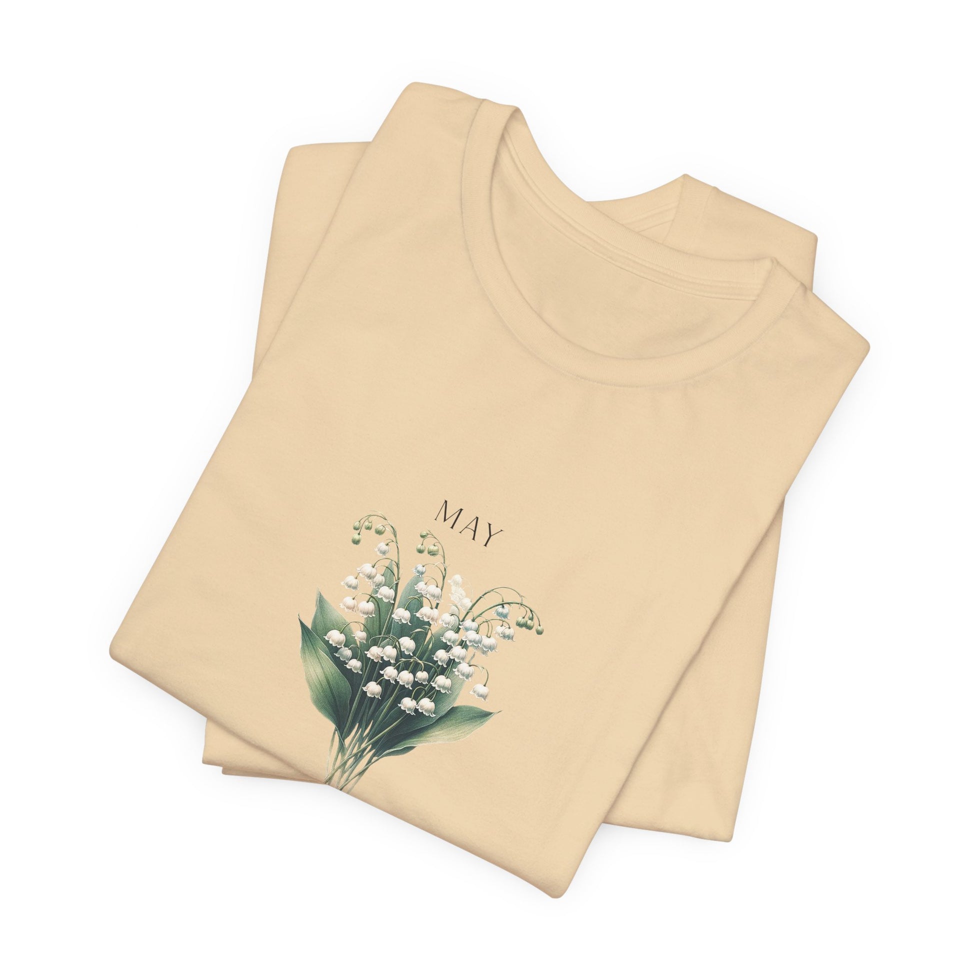 A t-shirt featuring a beautiful Lily of the Valley for May with traits Motherhood, Sweetness, Purity. Perfect for May birthdays and floral art lovers. Comfortable and stylish for casual outings or celebrations. Bella+Canvas 3001 t-shirt in soft cream. ReadyShirtAim.com