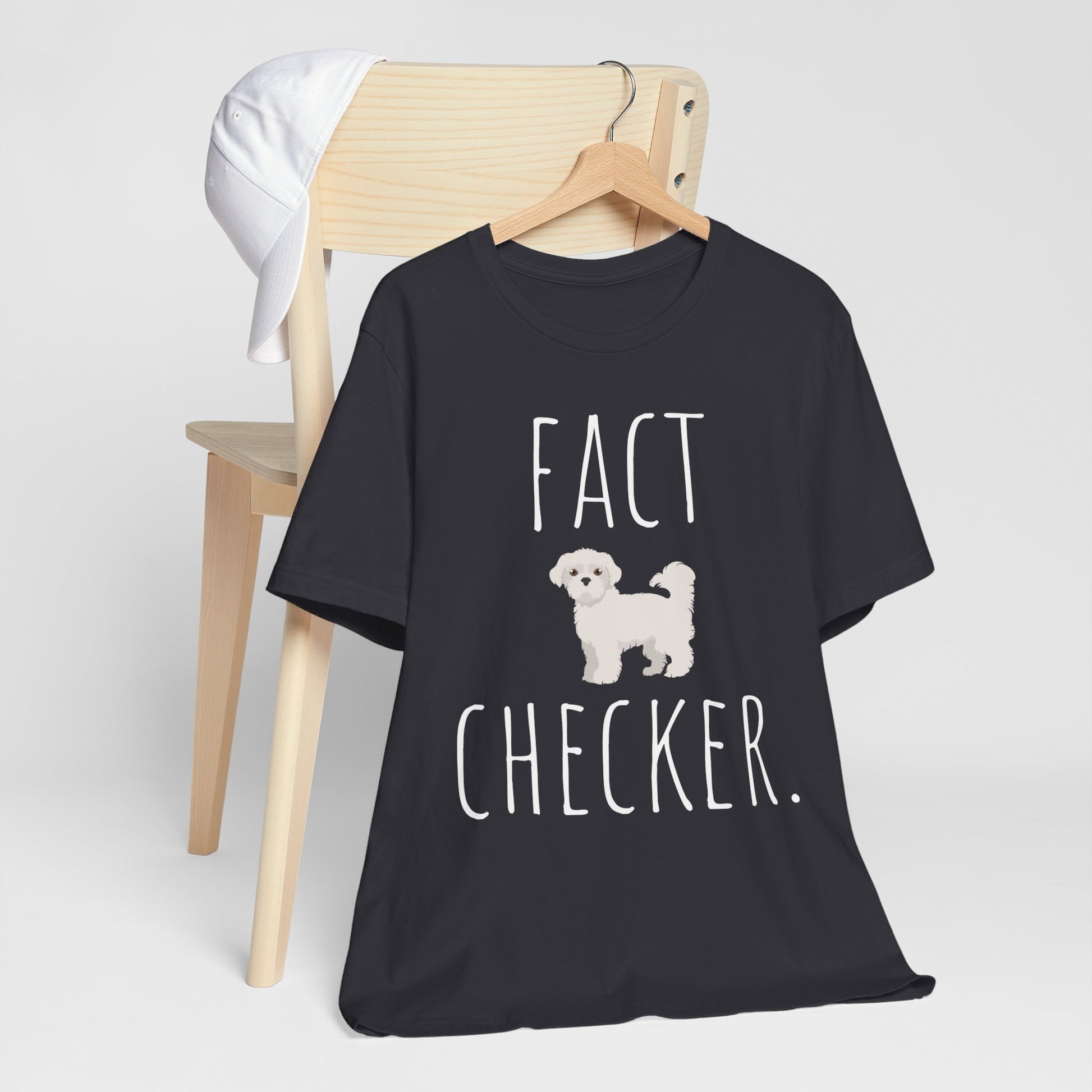 "Fact Checker" Maltese Dog T-Shirt for Unisex with a cute graphic of a Maltese dog and playful "Fact Checker" text underneath. Ideal for dog lovers. Ideal for dog lovers with a sense of humor. Available in multiple colors and sizes. Bella+Canvas 3001 t-shirt in dark grey. ReadyShirtAim.com