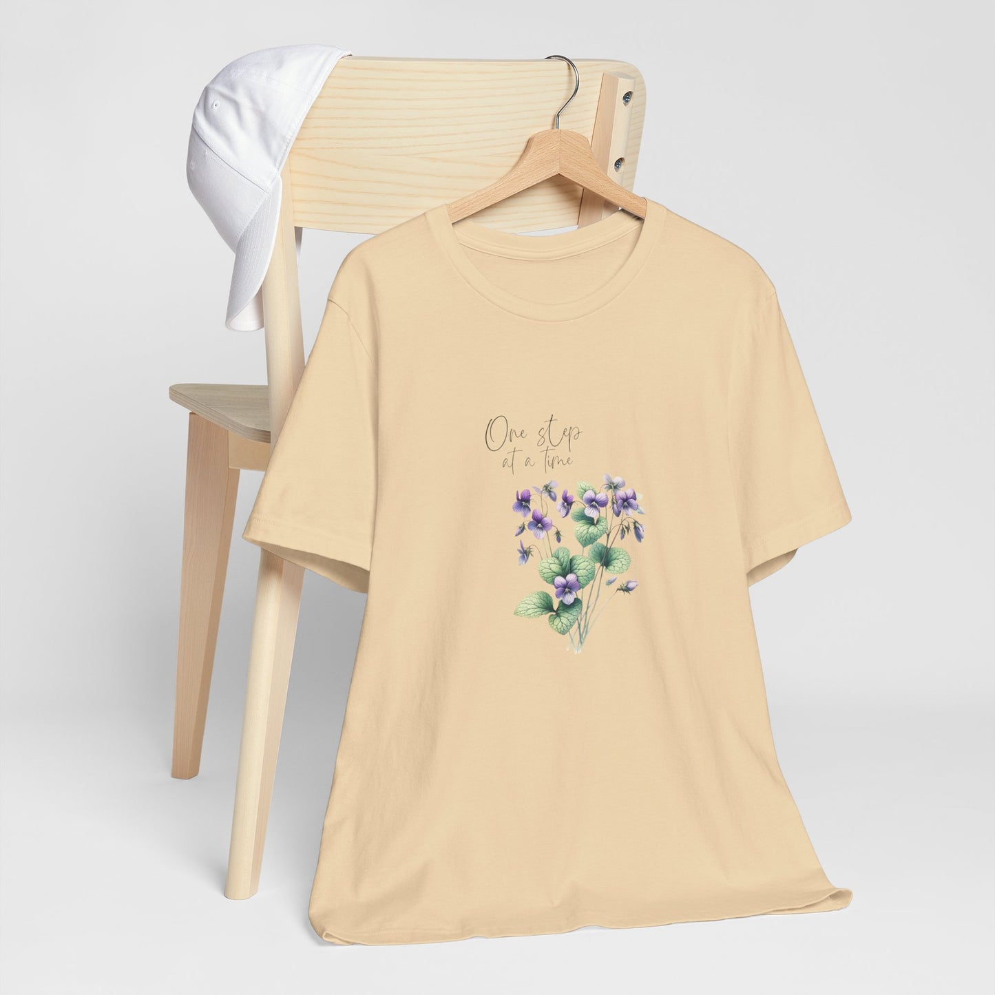 A t-shirt featuring a beautiful violet for February with the quote “One step at a time.” Perfect for February birthdays and floral art lovers. Comfortable and stylish for casual outings or celebrations. Bella+Canvas 3001 t-shirt in soft cream. ReadyShirtAim.com