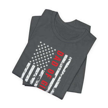 A dark-colored t-shirt featuring a grungy American flag design with the text "Dad of girls #outnumbered" in white and red. Perfect for Father's Day, Fourth of July, and patriotic dads who love humor. Comfortable and stylish for casual wear. Bella+Canvas 3001 t-shirt in asphalt. ReadyShirtAim.com