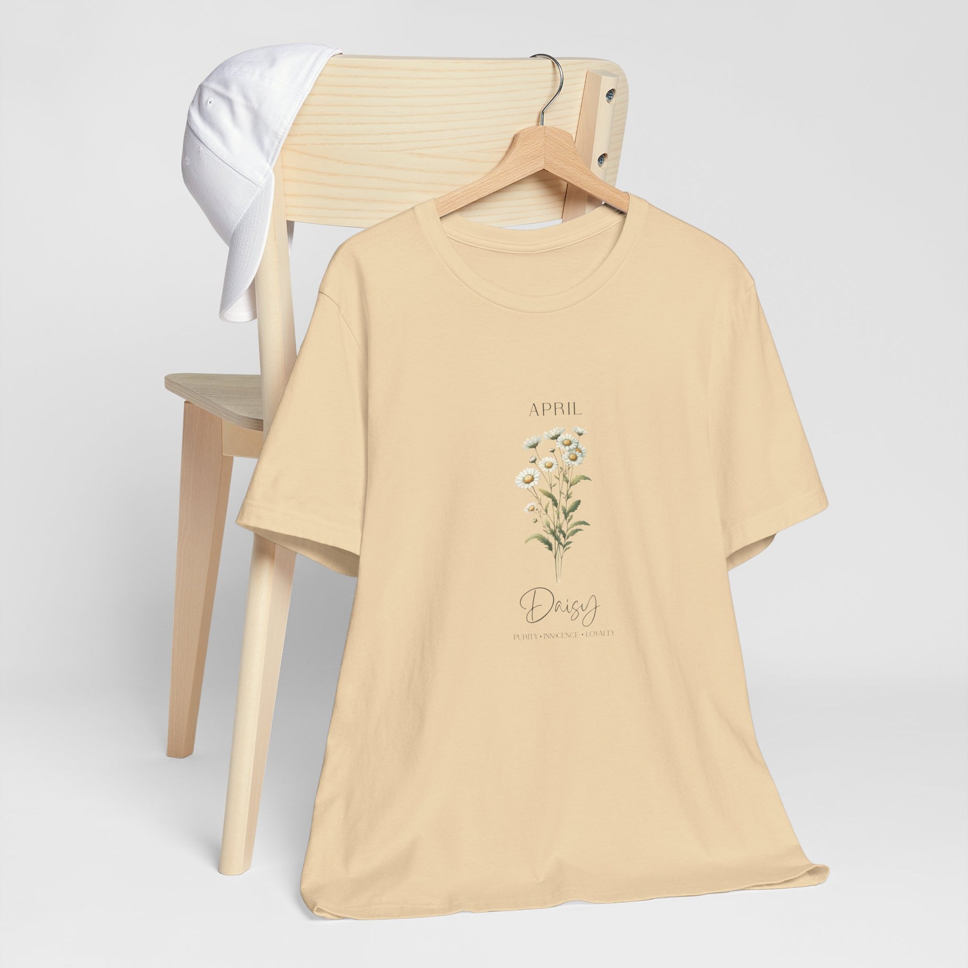 A t-shirt featuring a beautiful daisy for April with traits Purity, Innocence, Loyalty. Perfect for April birthdays and floral art lovers. Comfortable and stylish for casual outings or celebrations. Bella+Canvas 3001 t-shirt in soft cream. ReadyShirtAim.com