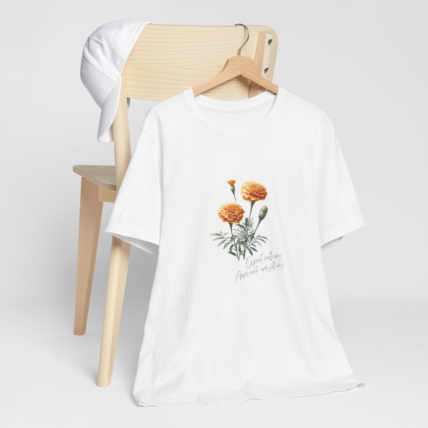 A t-shirt featuring a beautiful marigold for October with the quote “Expect nothing, appreciate everything.” Perfect for October birthdays and floral art lovers. Comfortable and stylish for casual outings or celebrations. Bella+Canvas 3001 t-shirt in white. ReadyShirtAim.com