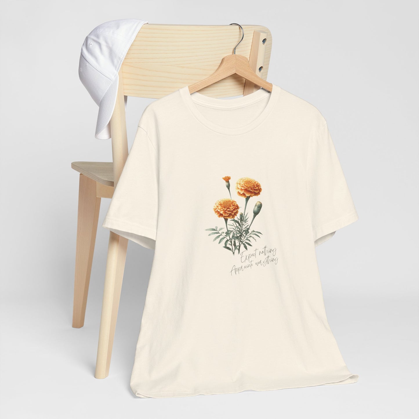 A t-shirt featuring a beautiful marigold for October with the quote “Expect nothing, appreciate everything.” Perfect for October birthdays and floral art lovers. Comfortable and stylish for casual outings or celebrations. Bella+Canvas 3001 t-shirt in natural. ReadyShirtAim.com