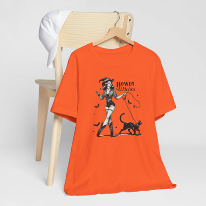 "Howdy Witches" Vintage 1950's Witch Halloween Women's T-Shirt featuring bold black text and a classic black-and-white image of a pin-up girl in sexy shorts and a western-style shirt, walking a black cat on a leash and smiling mischievously, perfect for adding a retro touch with playful Western charm to your Halloween festivities. Available in multiple colors and sizes.  Bella+Canvas 3001 t-shirt in orange. ReadyShirtAim.com