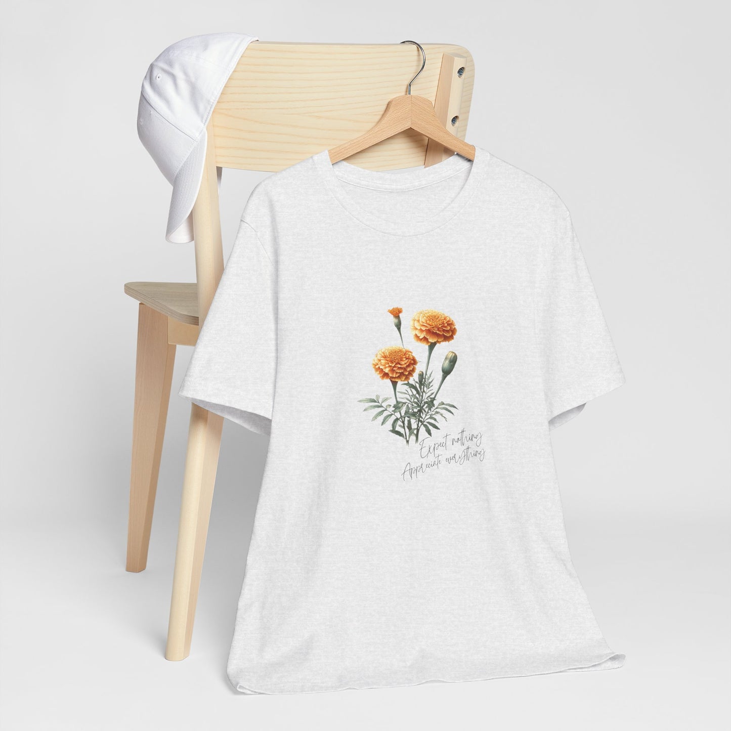 A t-shirt featuring a beautiful marigold for October with the quote “Expect nothing, appreciate everything.” Perfect for October birthdays and floral art lovers. Comfortable and stylish for casual outings or celebrations. Bella+Canvas 3001 t-shirt in ash. ReadyShirtAim.com