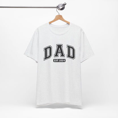 A stylish light colored t-shirt featuring the text "Dad Est. 2024" in a collegiate, sporty font, perfect for new fathers. Made from soft, breathable cotton, this shirt is an ideal gift for Father's Day or to celebrate a newborn's arrival. Available in multiple colors and sizes. Bella+Canvas 3001 t-shirt. ReadyShirtAim.com