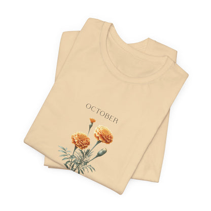 A t-shirt featuring a beautiful marigold for October with traits Passion, Creativity, Courage. Perfect for October birthdays and floral art lovers. Comfortable and stylish for casual outings or celebrations. Bella+Canvas 3001 t-shirt in soft cream. ReadyShirtAim.com