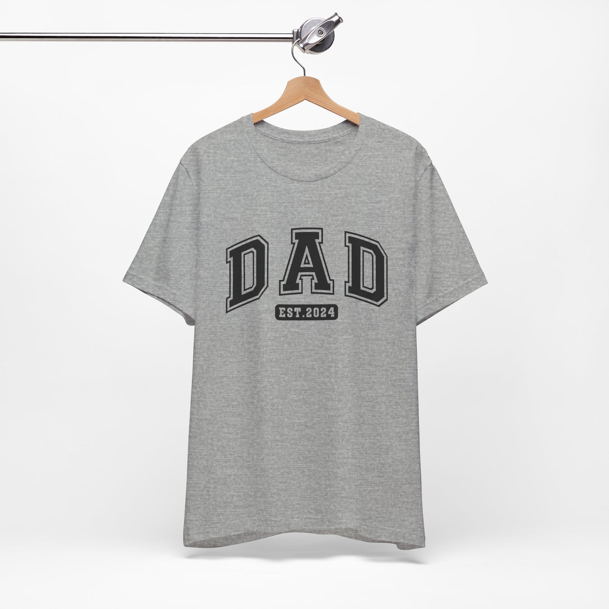 A stylish light colored t-shirt featuring the text "Dad Est. 2024" in a collegiate, sporty font, perfect for new fathers. Made from soft, breathable cotton, this shirt is an ideal gift for Father's Day or to celebrate a newborn's arrival. Available in multiple colors and sizes. Bella+Canvas 3001 t-shirt. ReadyShirtAim.com