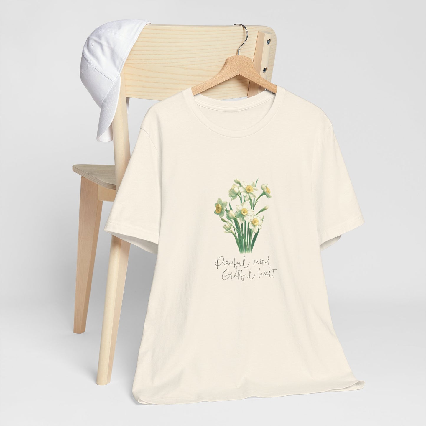 A t-shirt featuring a beautiful narcissus for December with the quote “Peaceful mind, grateful heart.” Perfect for December birthdays and floral art lovers. Comfortable and stylish for casual outings or celebrations. Bella+Canvas 3001 t-shirt in natural. ReadyShirtAim.com