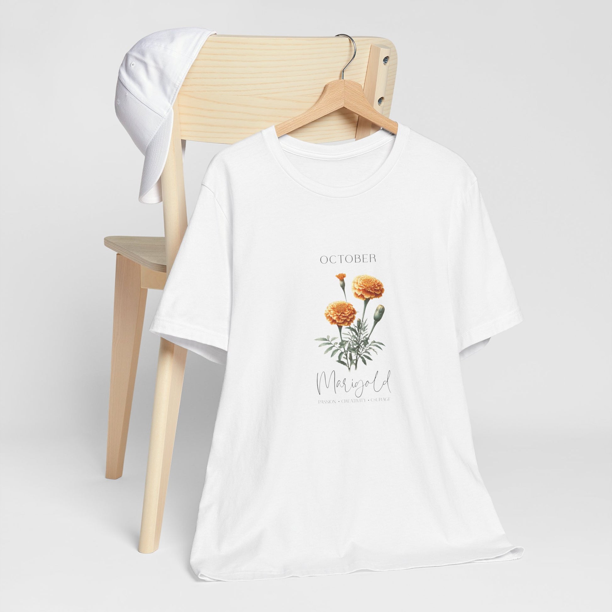 A t-shirt featuring a beautiful marigold for October with traits Passion, Creativity, Courage. Perfect for October birthdays and floral art lovers. Comfortable and stylish for casual outings or celebrations. Bella+Canvas 3001 t-shirt in white. ReadyShirtAim.com