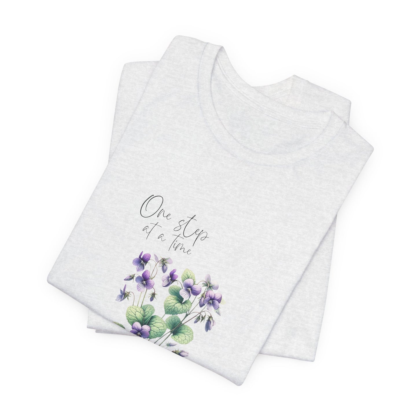 A t-shirt featuring a beautiful violet for February with the quote “One step at a time.” Perfect for February birthdays and floral art lovers. Comfortable and stylish for casual outings or celebrations. Bella+Canvas 3001 t-shirt in ash. ReadyShirtAim.com