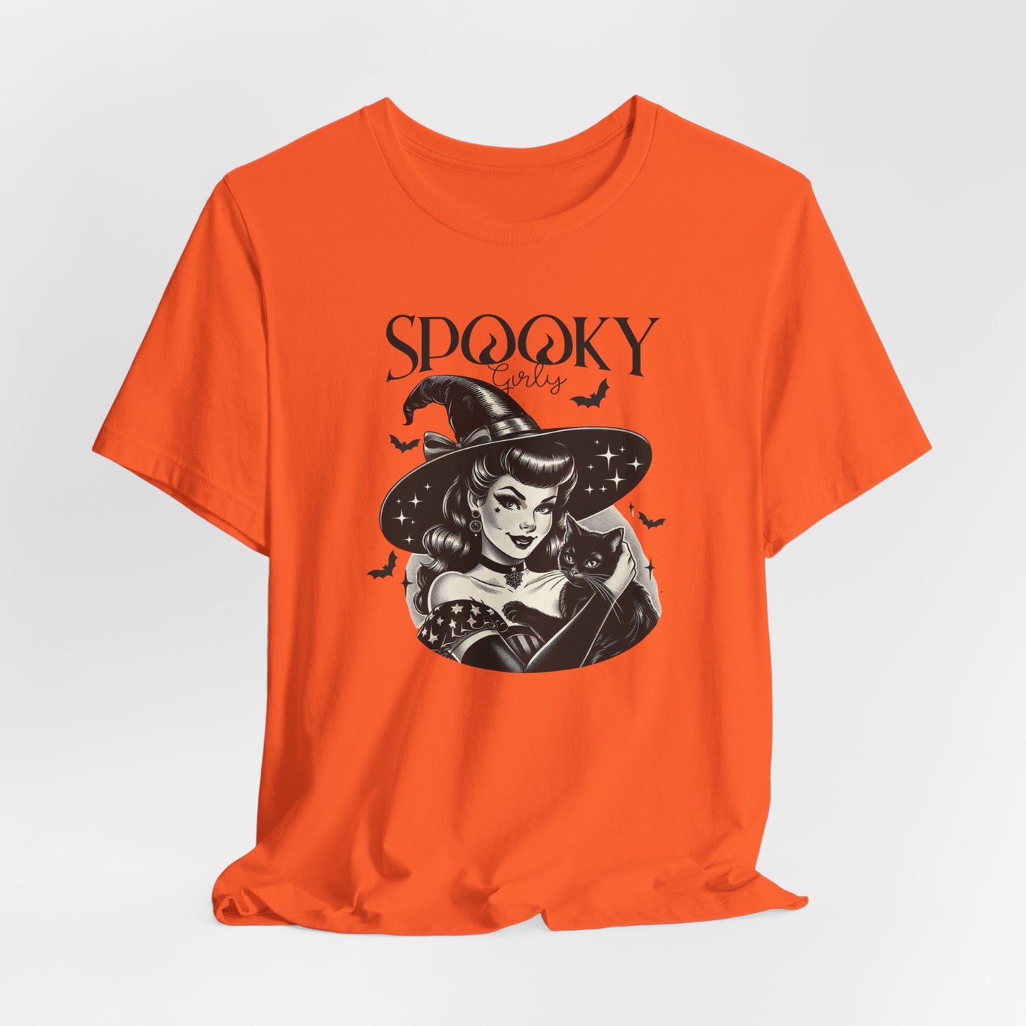 "Spooky Girly" Vintage 1950's Witch Halloween Women's T-Shirt featuring bold black text and a classic black-and-white image of a pin-up girl in a sexy witch costume, holding a black cat and smiling mischievously, perfect for adding a retro touch with playful charm to your Halloween festivities. Available in multiple colors and sizes.  Bella+Canvas 3001 t-shirt in orange. ReadyShirtAim.com