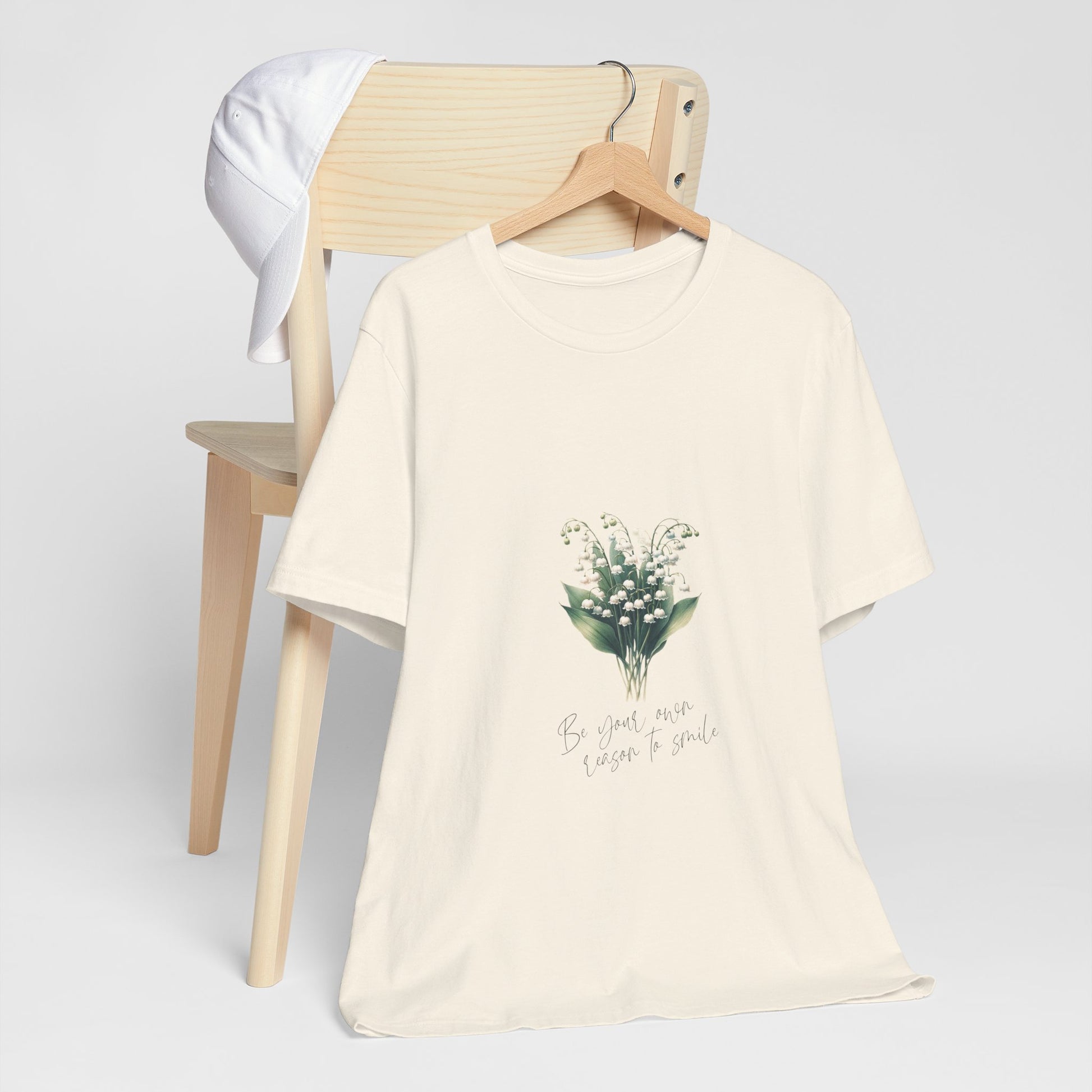 A t-shirt featuring a beautiful Lily of the Valley for May with the quote “Be your own reason to smile.” Perfect for May birthdays and floral art lovers. Comfortable and stylish for casual outings or celebrations. Bella+Canvas 3001 t-shirt in natural. ReadyShirtAim.com