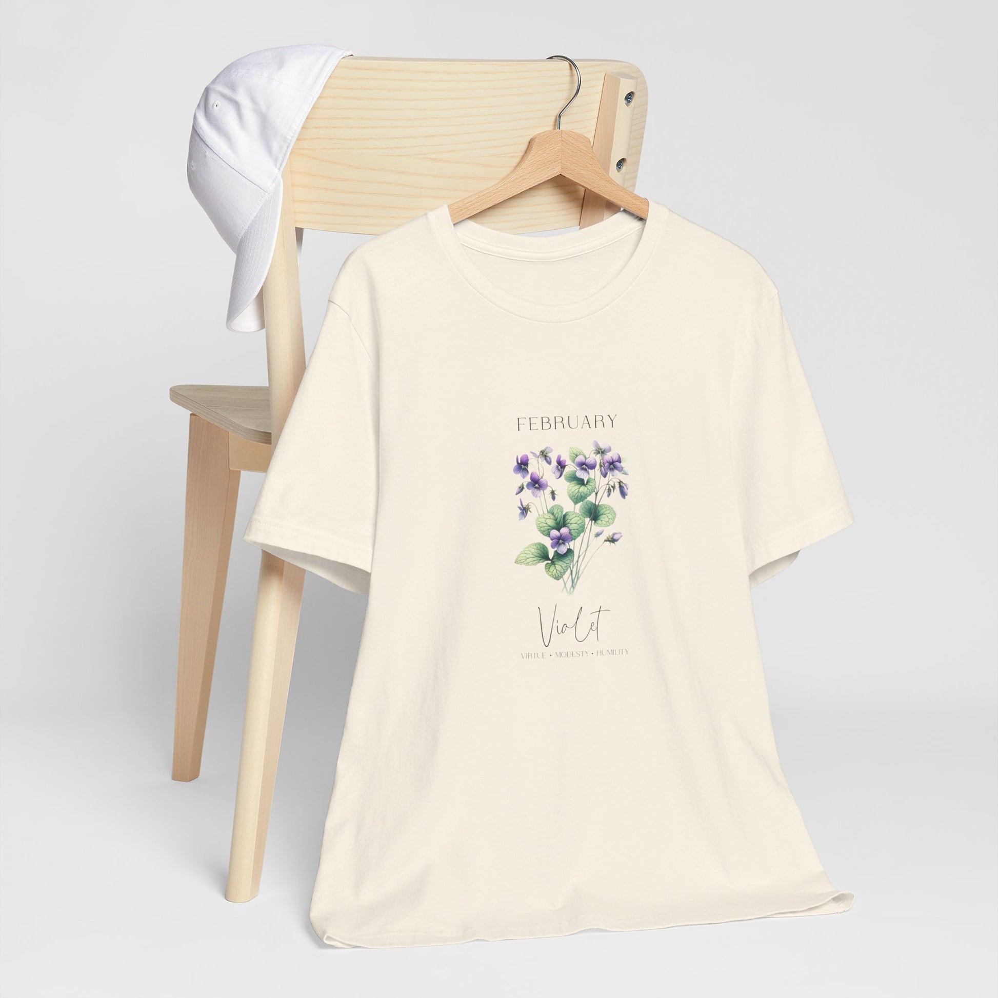 A t-shirt featuring a beautiful violet for February with traits Virtue, Modesty, Humility. Perfect for February birthdays and floral art lovers. Comfortable and stylish for casual outings or celebrations. Bella+Canvas 3001 t-shirt in natural. ReadyShirtAim.com