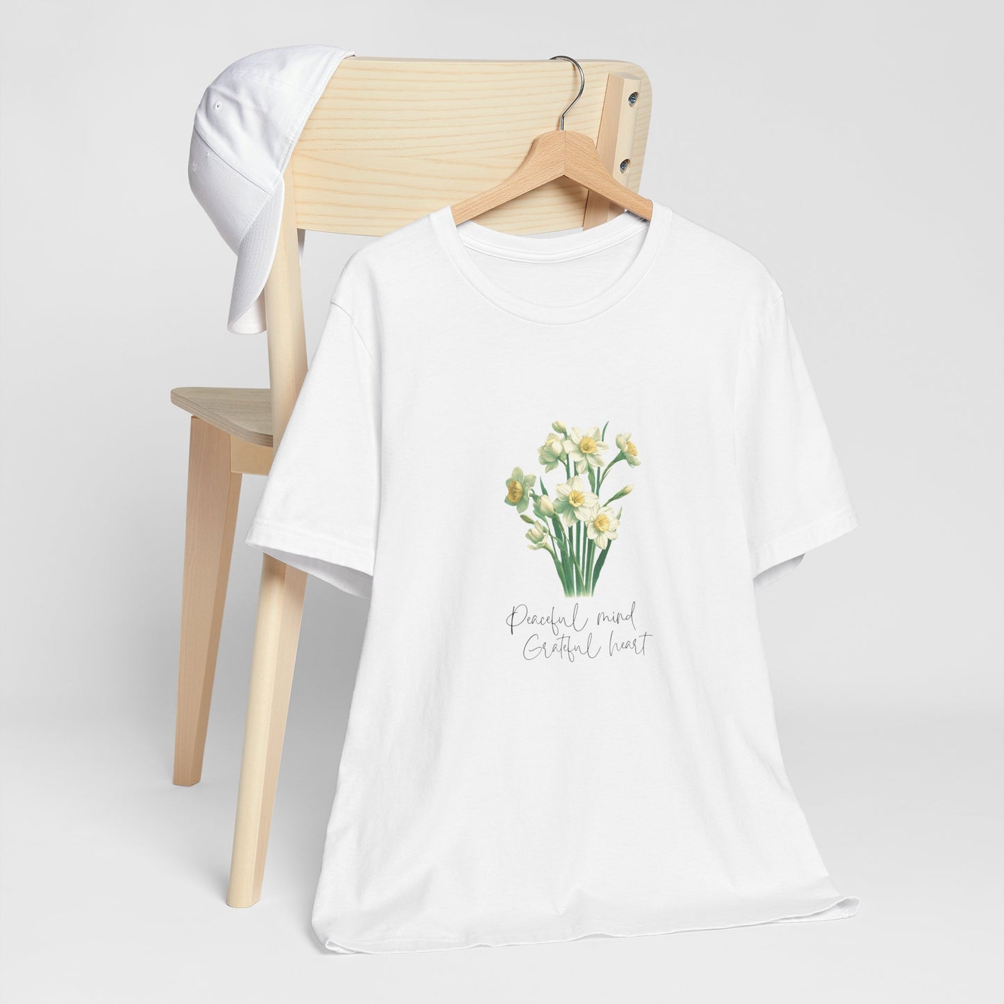 A t-shirt featuring a beautiful narcissus for December with the quote “Peaceful mind, grateful heart.” Perfect for December birthdays and floral art lovers. Comfortable and stylish for casual outings or celebrations. Bella+Canvas 3001 t-shirt in white. ReadyShirtAim.com