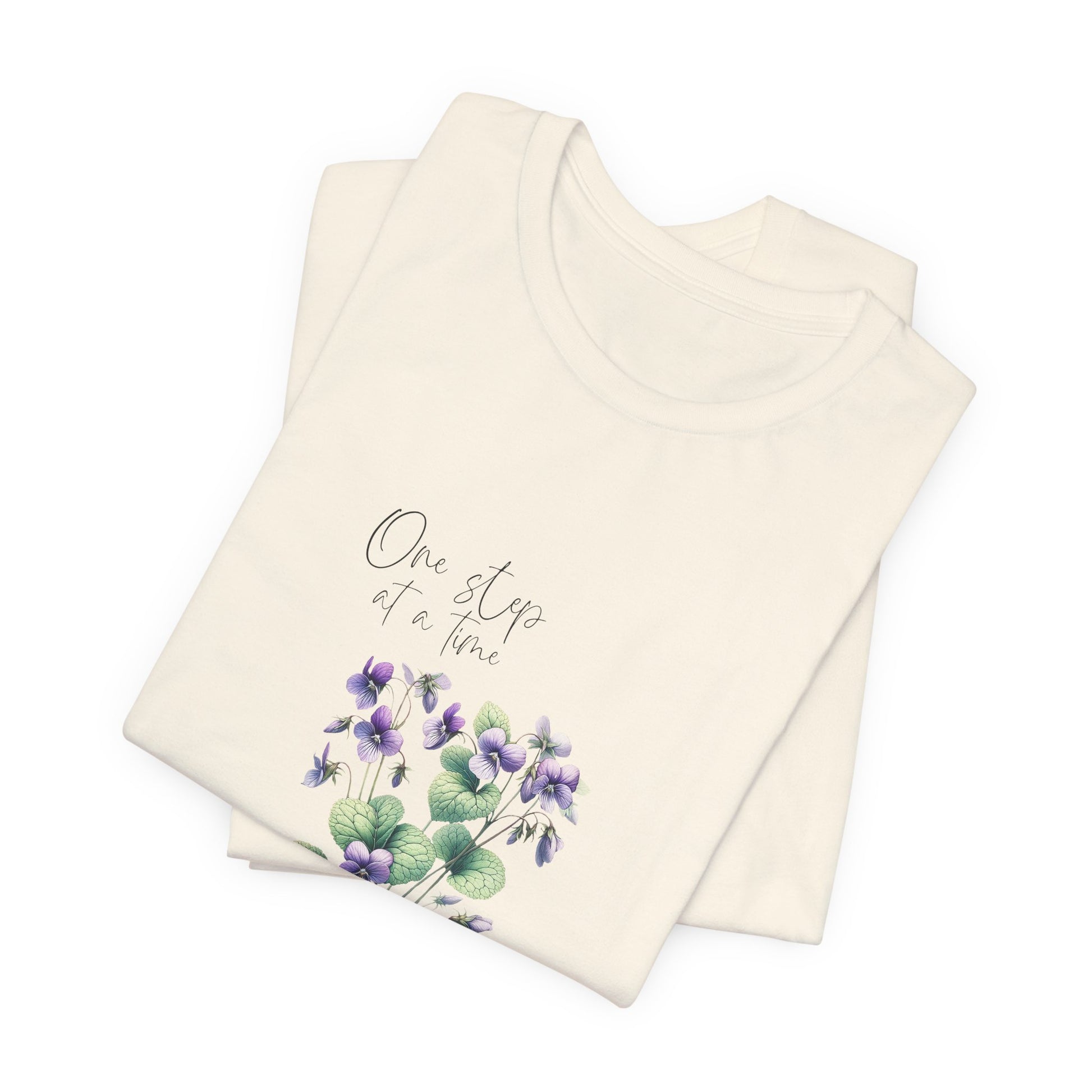 A t-shirt featuring a beautiful violet for February with the quote “One step at a time.” Perfect for February birthdays and floral art lovers. Comfortable and stylish for casual outings or celebrations. Bella+Canvas 3001 t-shirt in natural. ReadyShirtAim.com