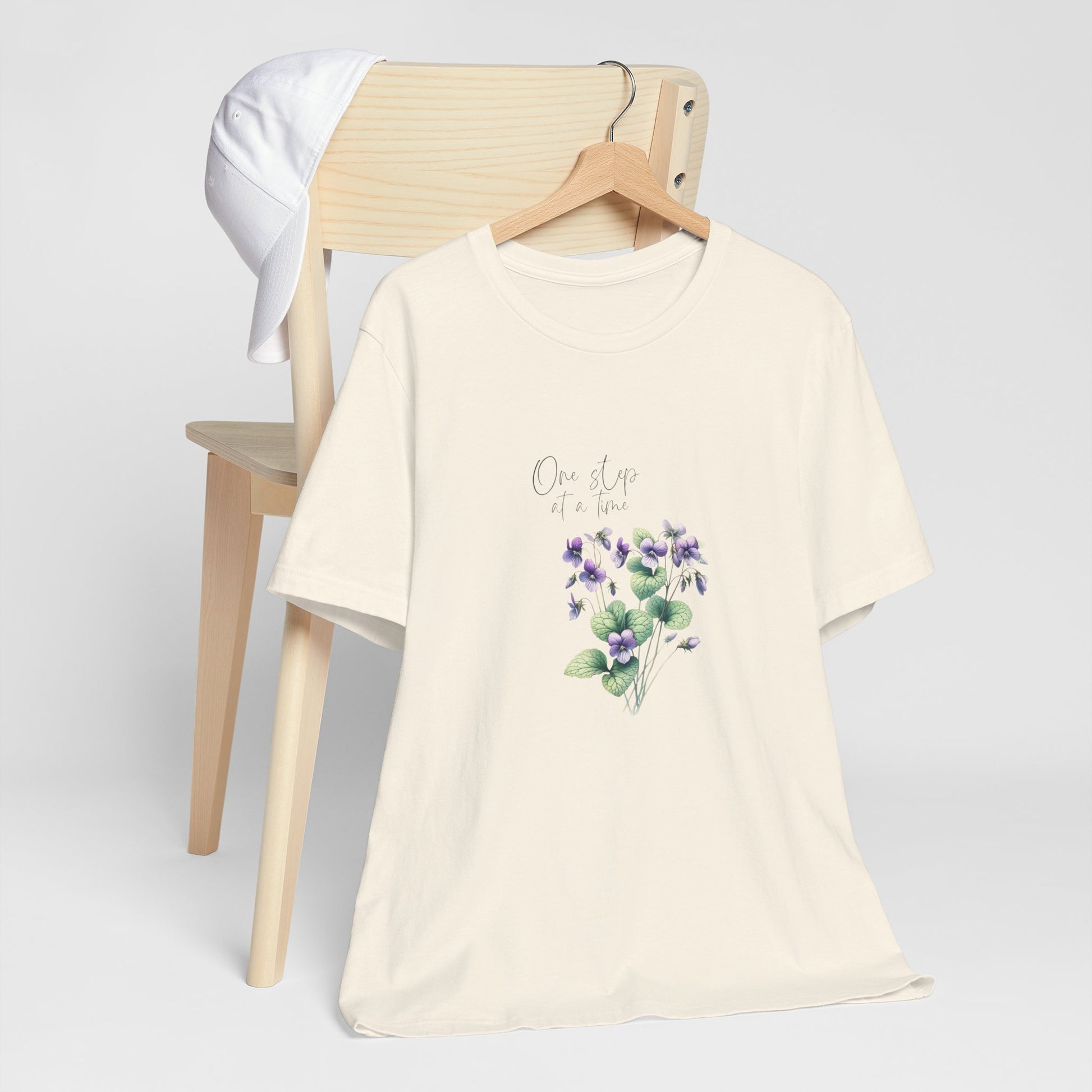 A t-shirt featuring a beautiful violet for February with the quote “One step at a time.” Perfect for February birthdays and floral art lovers. Comfortable and stylish for casual outings or celebrations. Bella+Canvas 3001 t-shirt in natural. ReadyShirtAim.com