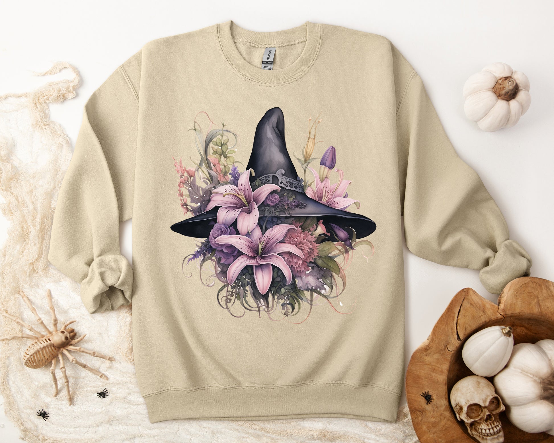 Charming Witch Hat & Flowers Sweatshirt with a watercolor illustration of a black witch hat and flowers in purple, pink, and green. Available in multiple dark and light colors and sizes. Gildan 18000 sweatshirt in Sand. ReadyShirtAim.com