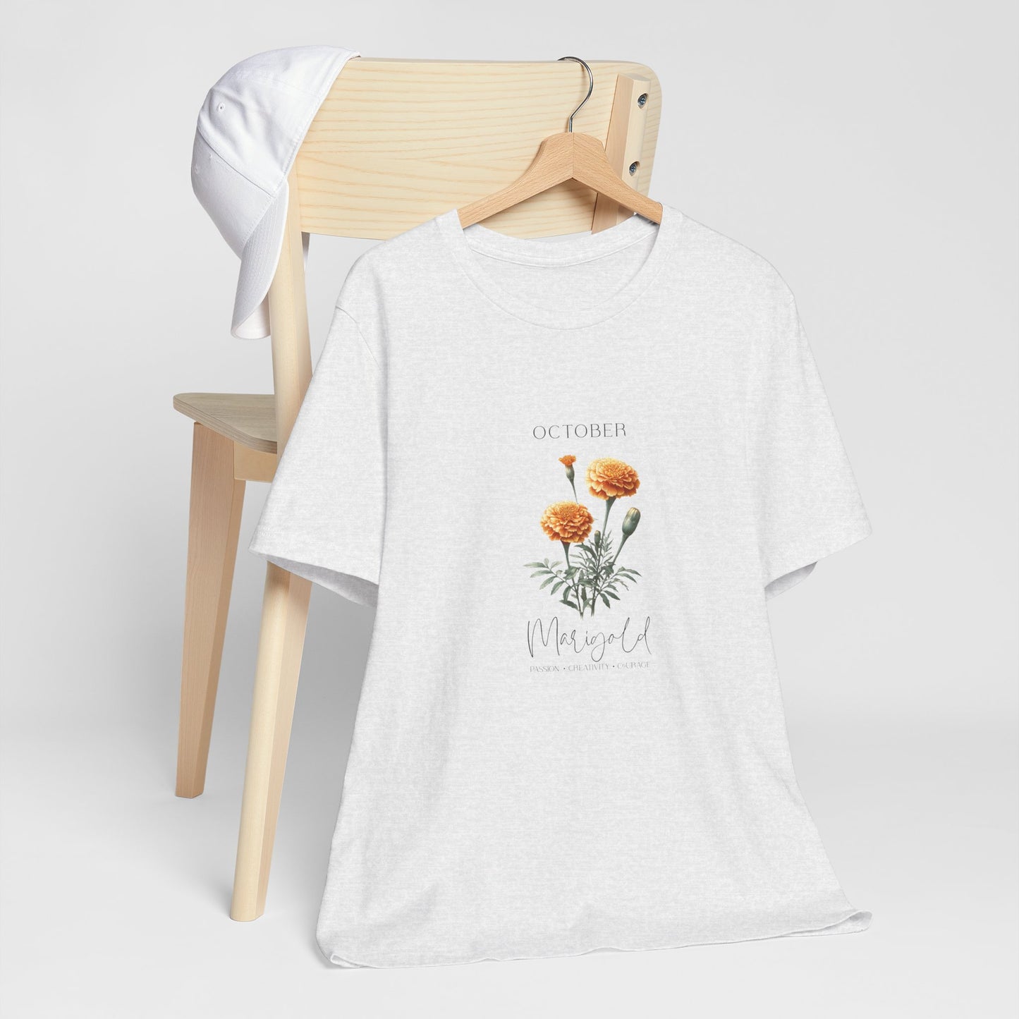 A t-shirt featuring a beautiful marigold for October with traits Passion, Creativity, Courage. Perfect for October birthdays and floral art lovers. Comfortable and stylish for casual outings or celebrations. Bella+Canvas 3001 t-shirt in ash. ReadyShirtAim.com