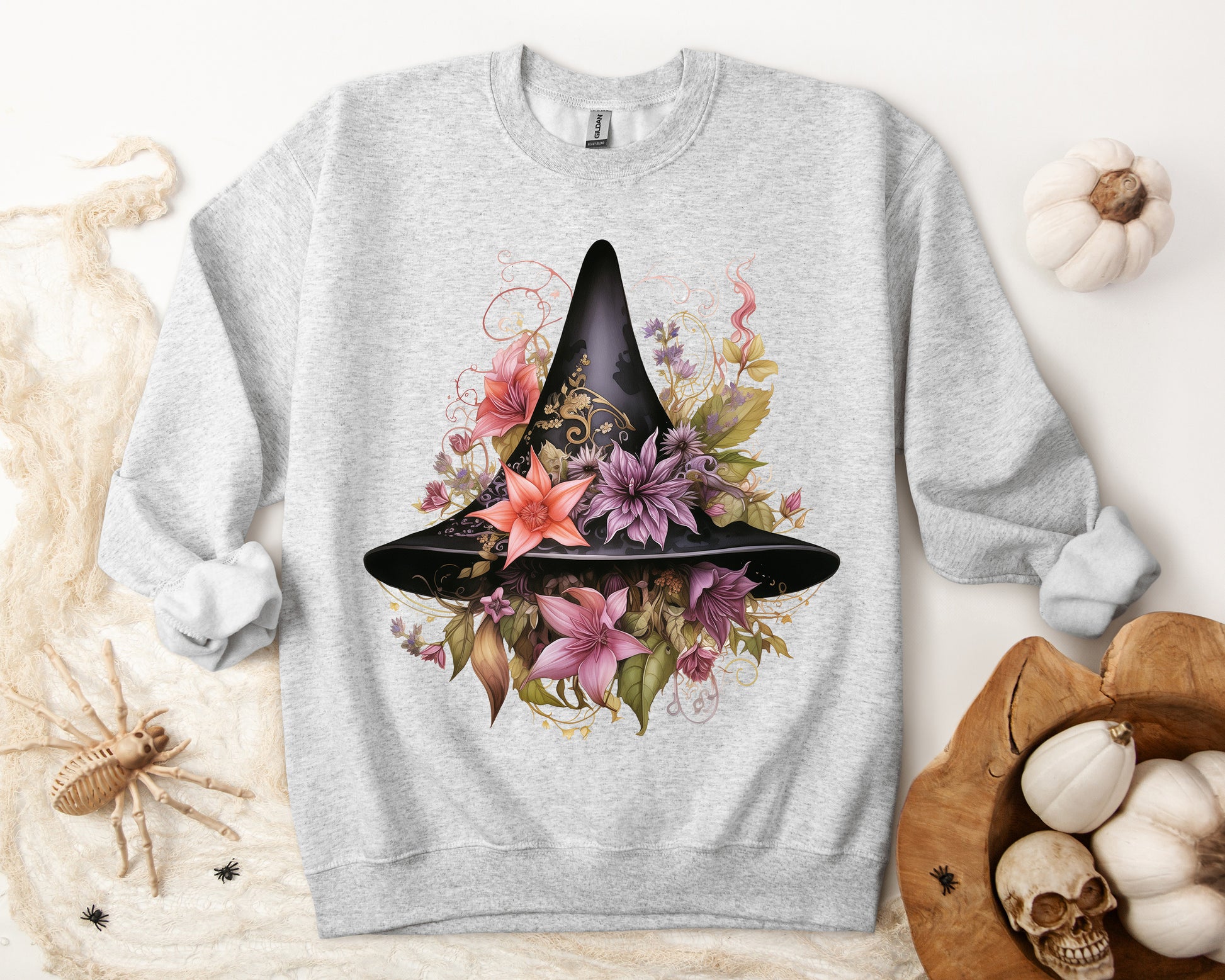 Whimsical Witch Hat Sweatshirt with a watercolor illustration of a black witch hat surrounded by flowers in purple, pink, and green. Available in multiple dark and light colors and sizes. Gildan 18000 sweatshirt in ash. ReadyShirtAim.com