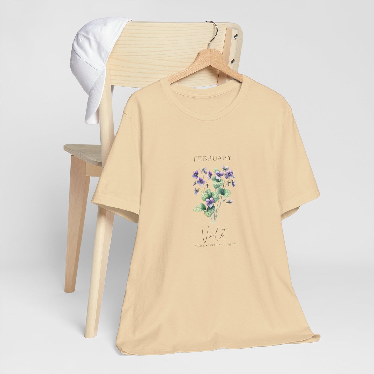 A t-shirt featuring a beautiful violet for February with traits Virtue, Modesty, Humility. Perfect for February birthdays and floral art lovers. Comfortable and stylish for casual outings or celebrations. Bella+Canvas 3001 t-shirt in soft cream. ReadyShirtAim.com