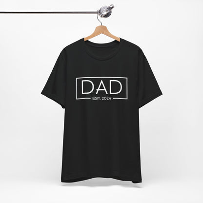 A dark t-shirt featuring the text "Dad Est. 2024" in a modern font, perfect for new fathers. Made from soft, breathable cotton, this shirt is an ideal gift for Father's Day or to celebrate a newborn's arrival. Available in multiple colors and sizes. Bella+Canvas 3001 t-shirt. ReadyShirtAim.com