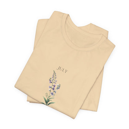 A t-shirt featuring a beautiful larkspur for July with traits Positive, Grace, First Love. Perfect for July birthdays and floral art lovers. Comfortable and stylish for casual outings or celebrations. Bella+Canvas 3001 t-shirt in soft cream. ReadyShirtAim.com