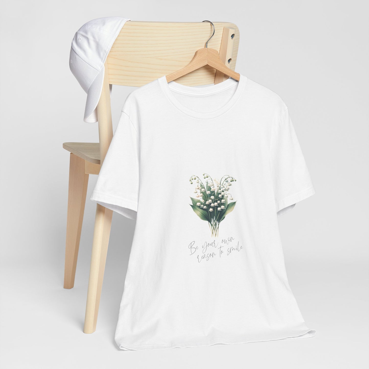 A t-shirt featuring a beautiful Lily of the Valley for May with the quote “Be your own reason to smile.” Perfect for May birthdays and floral art lovers. Comfortable and stylish for casual outings or celebrations. Bella+Canvas 3001 t-shirt in white. ReadyShirtAim.com