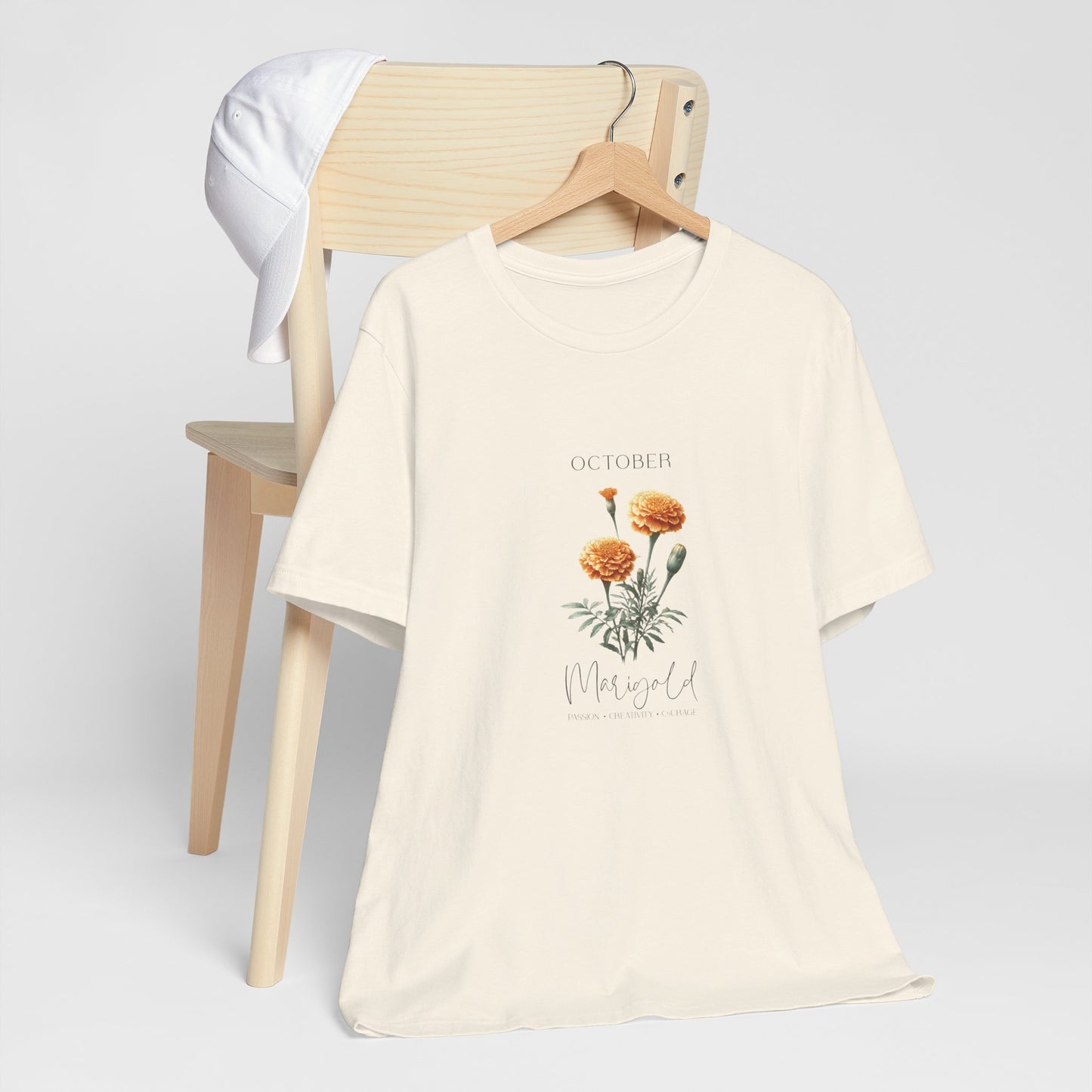 A t-shirt featuring a beautiful marigold for October with traits Passion, Creativity, Courage. Perfect for October birthdays and floral art lovers. Comfortable and stylish for casual outings or celebrations. Bella+Canvas 3001 t-shirt in natural. ReadyShirtAim.com